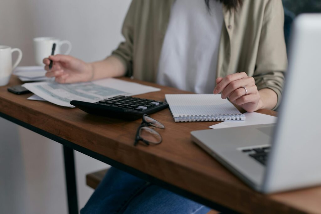 a person on a table with paper, laptop and calculator